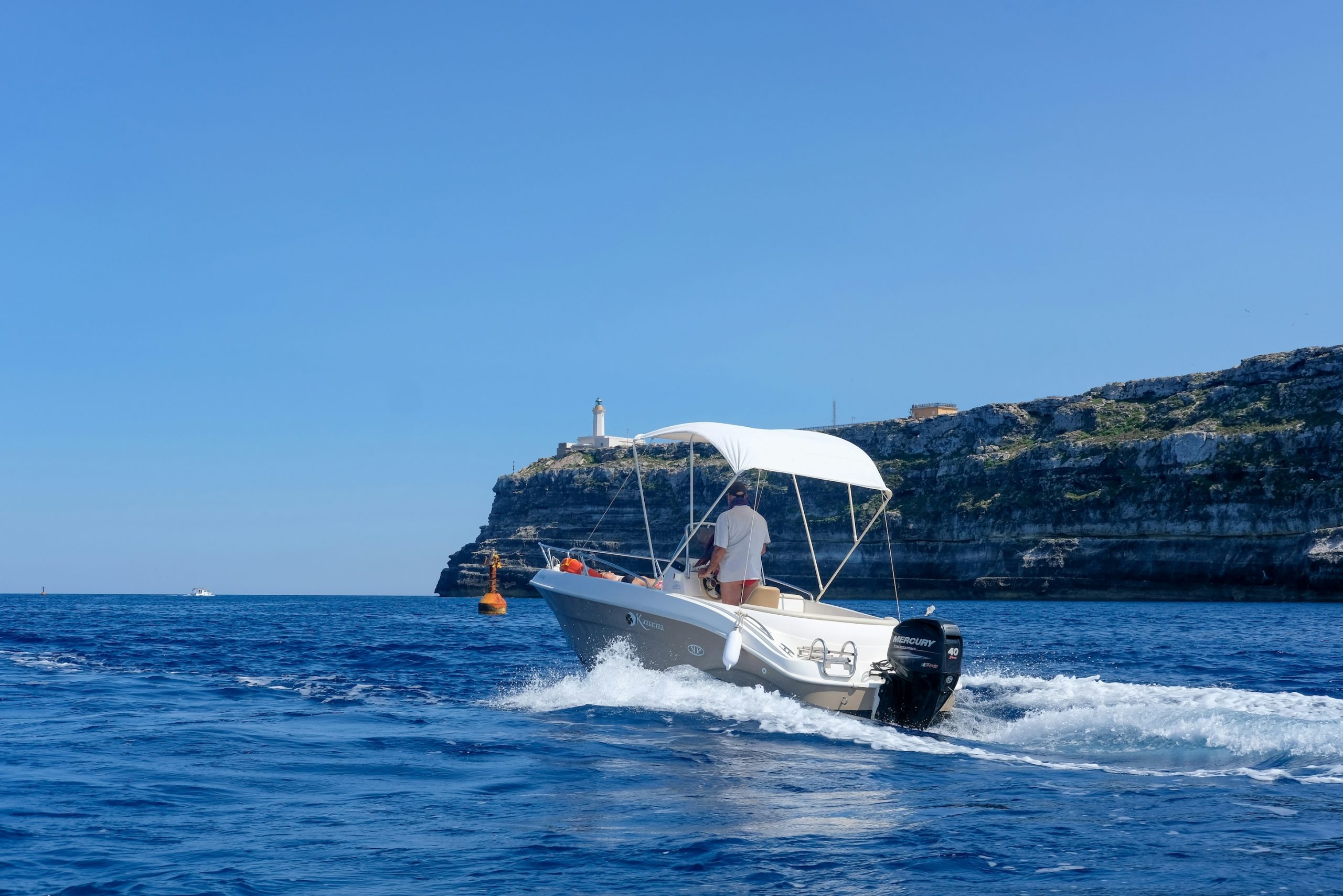 Una lancha blanca con toldo navegando por el mar con la costa al fondo. 